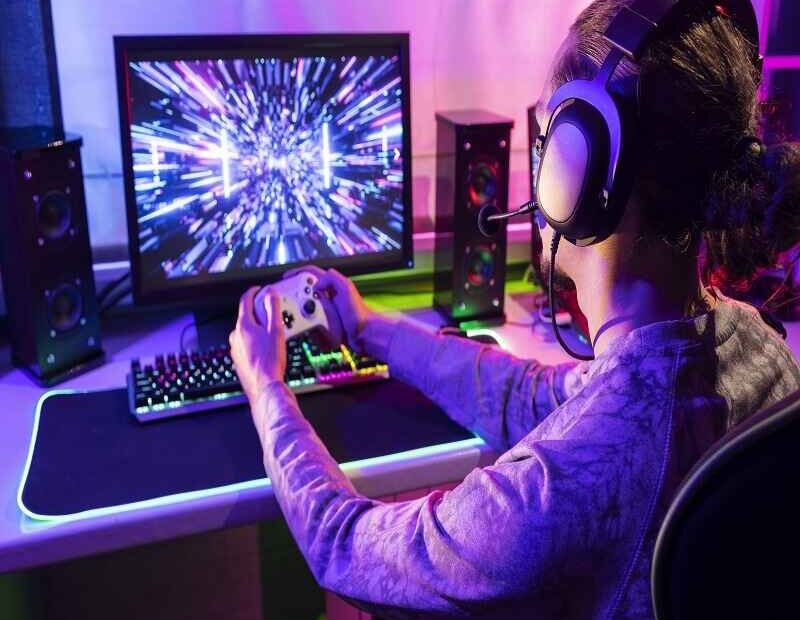 A gamer immersed in playing on a high-performance gaming setup with colorful visuals and a game controller, highlighting the interactive and immersive nature of modern gaming experiences.